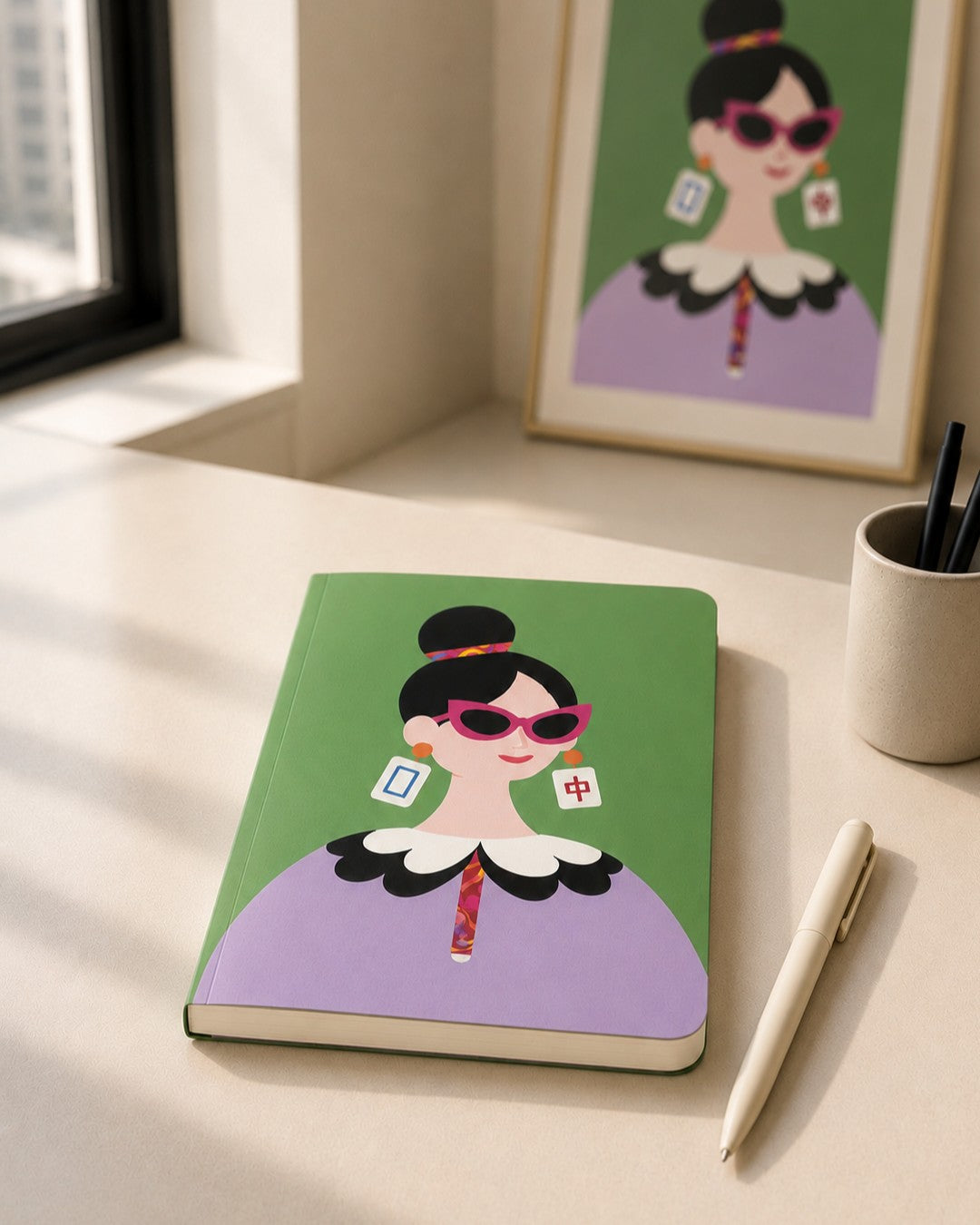 The Dragon Pair Journal displayed on a desk beside a pen, with a framed The Dragon Pair art print in the background